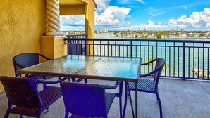 A balcony with a table and chairs, overlooking a waterfront with buildings in the background.