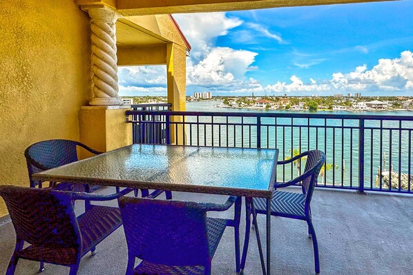 A balcony with a table and chairs, overlooking a waterfront with buildings in the background.