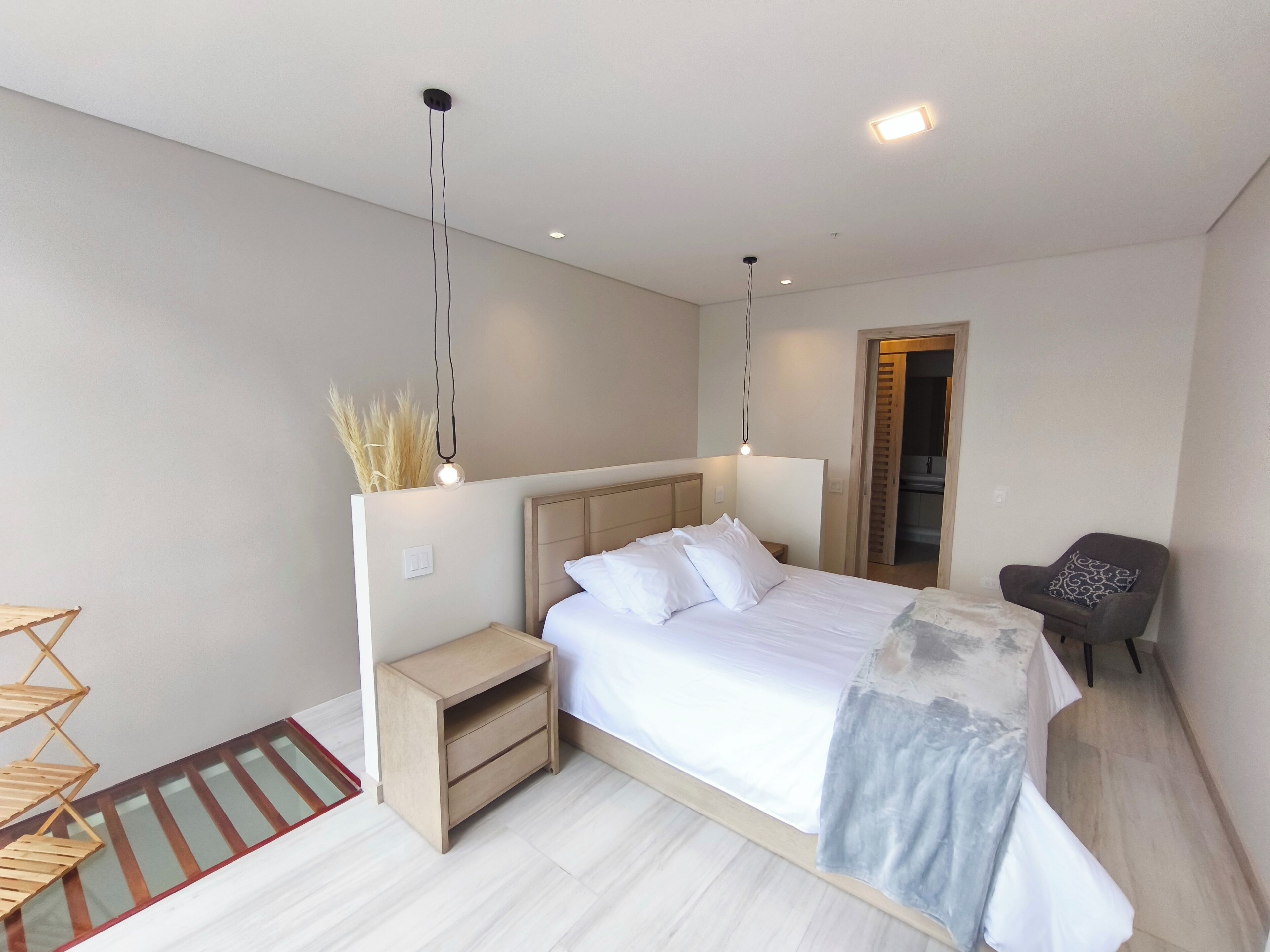 A modern bedroom with a large bed, bedside tables, a chair, and a small table with a lamp.