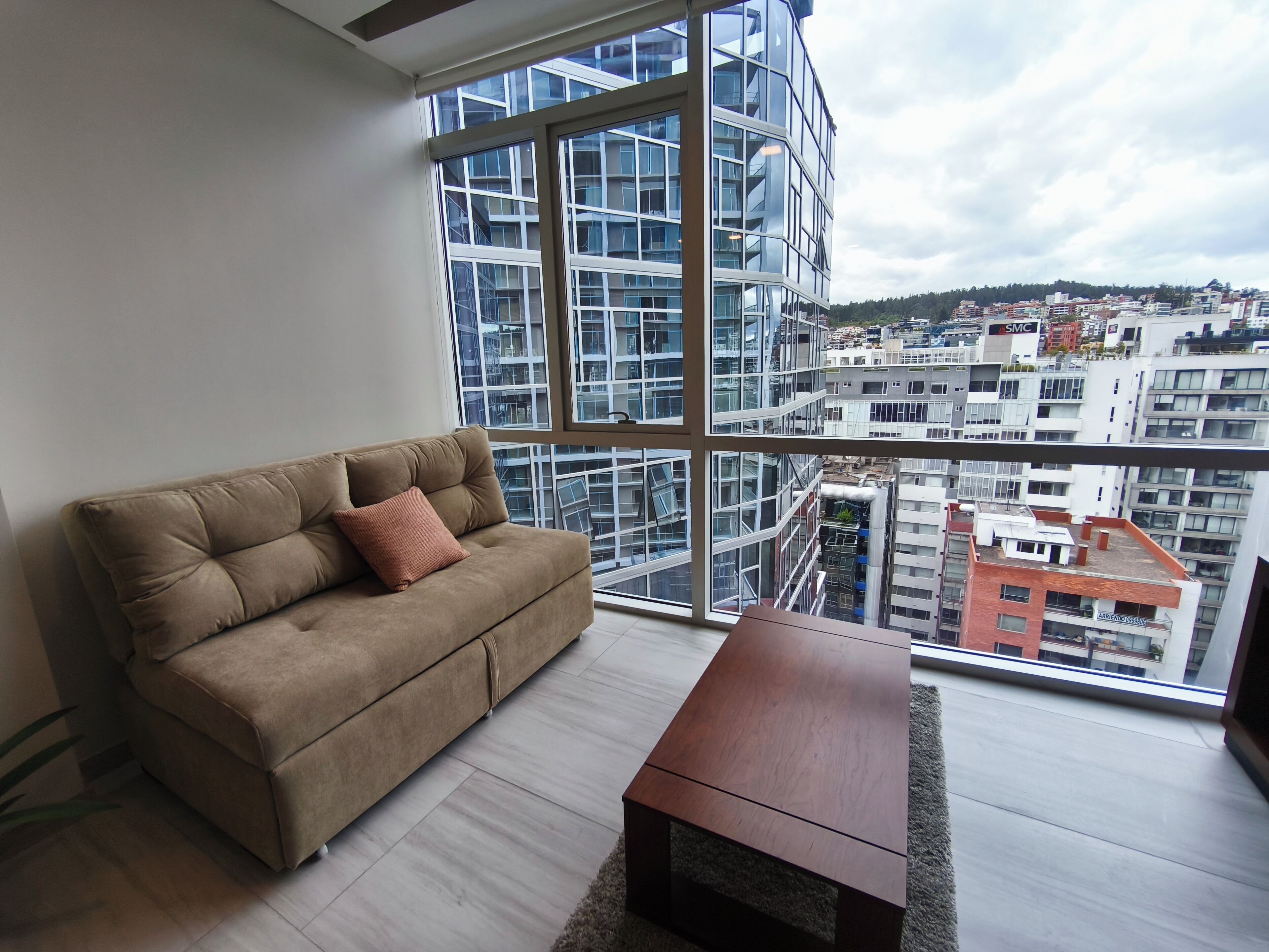 A modern living room with a large window, a beige sofa, and a wooden coffee table.