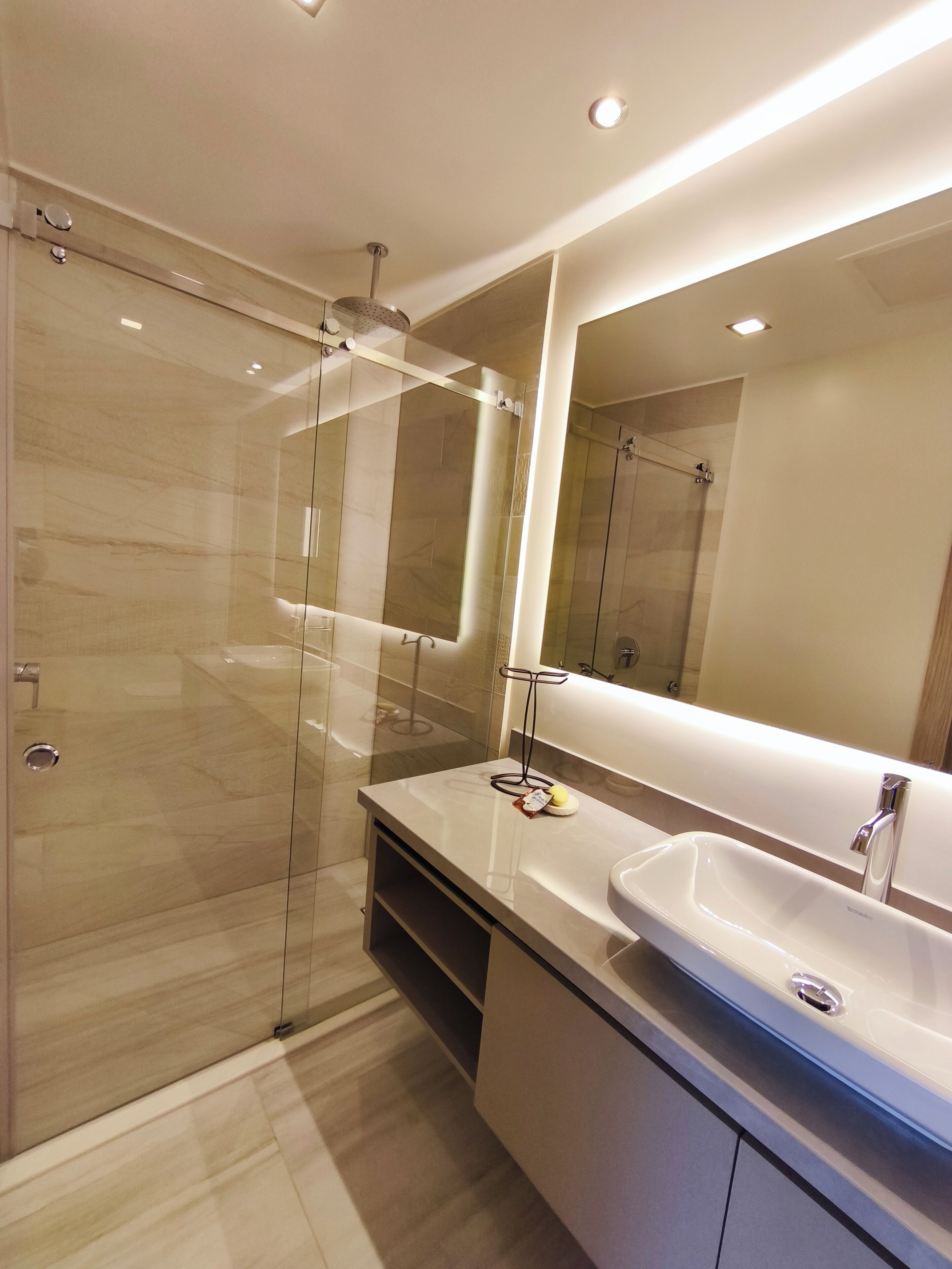 A modern bathroom with a glass shower enclosure, a large mirror, and a white sink.