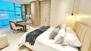 Une chambre moderne avec un grand lit, des tables de chevet, un bureau et une vue dégagée sur l’extérieur grâce à une grande fenêtre.