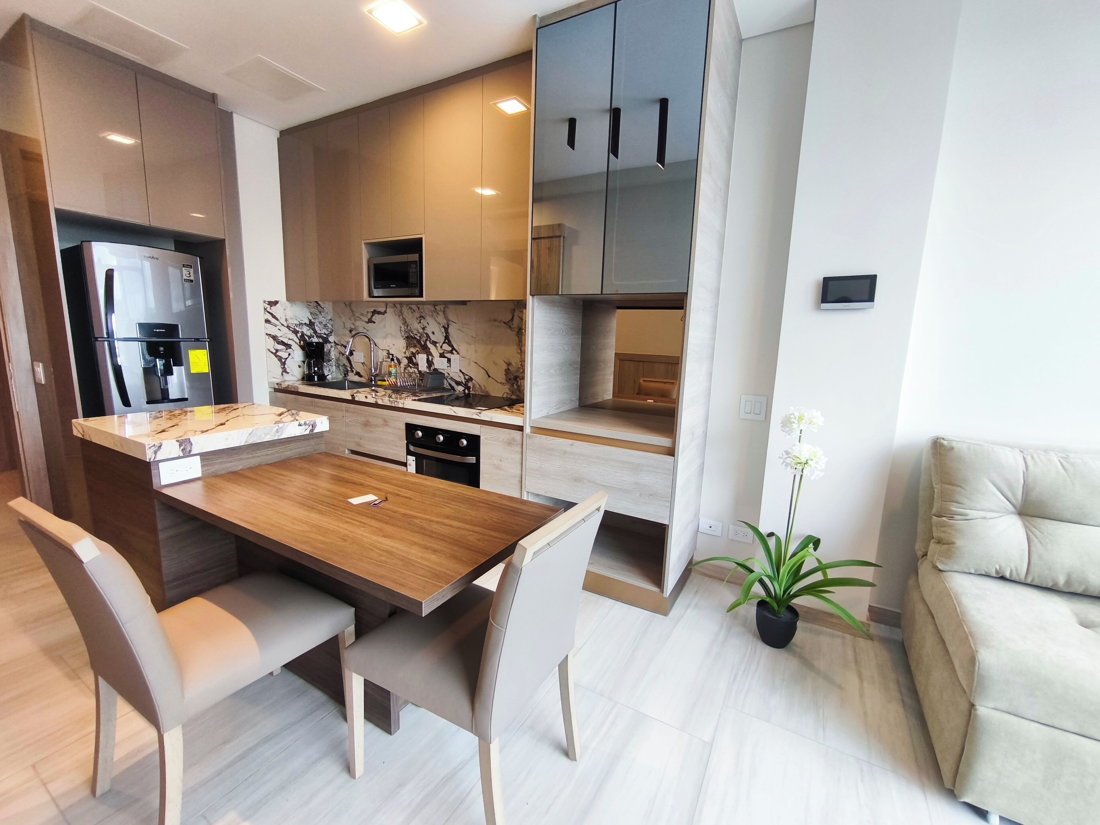 A modern kitchen with a wooden dining table and chairs, built-in appliances, and a marble backsplash.