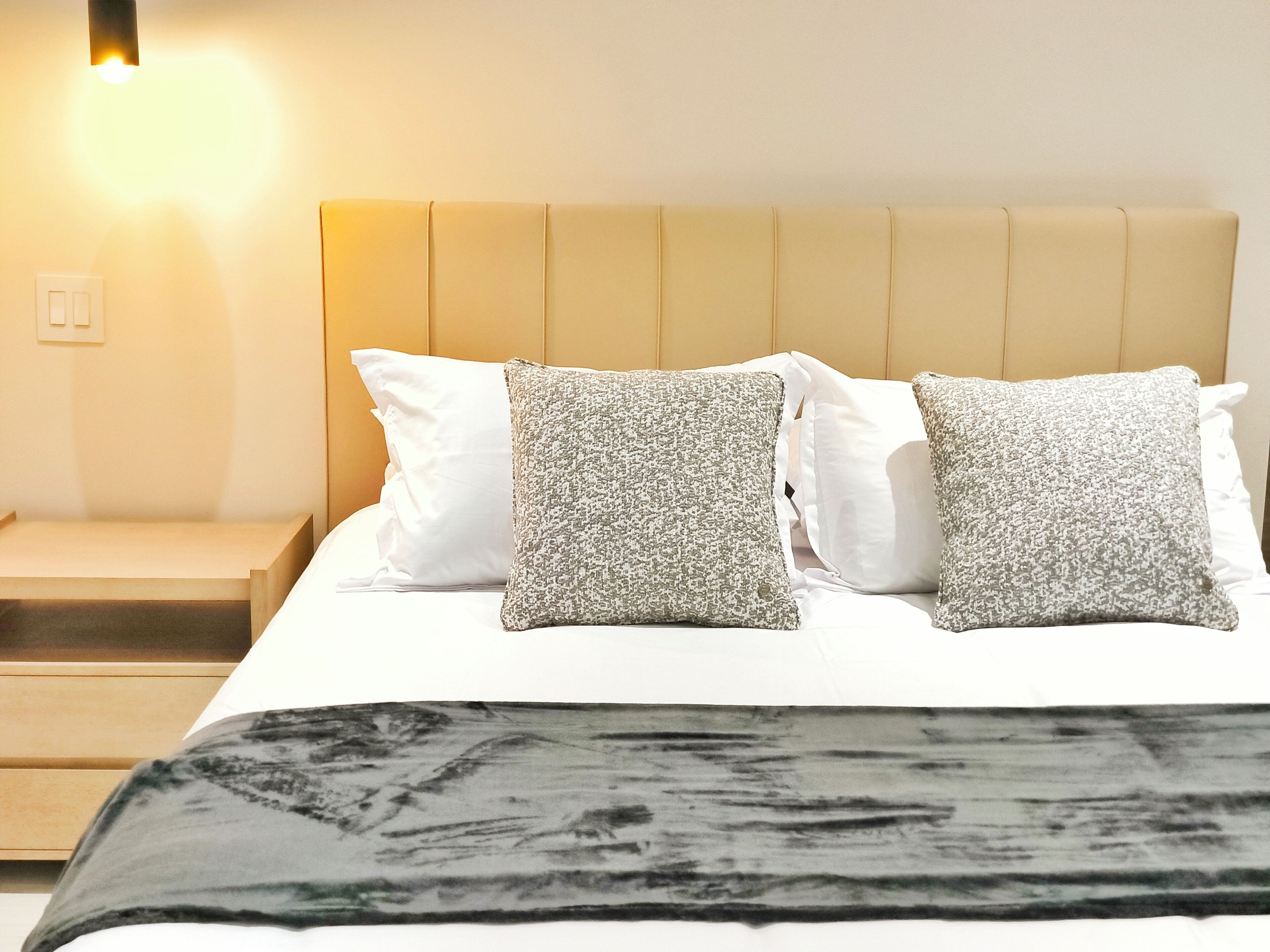 A neatly made bed with a headboard, two white pillows, and two patterned pillows.