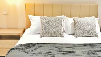 A neatly made bed with a headboard, two white pillows, and two patterned pillows.