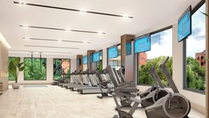 Une salle de sport moderne dotée de plusieurs tapis de course, de grandes fenêtres et d’un plancher en bois.