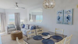 Une pièce comprenant une table à manger, des chaises, un ventilateur de plafond, un luminaire suspendu, un grand miroir et des œuvres d’art accrochées au mur.