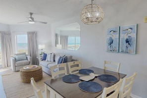 A room with a dining table, chairs, a ceiling fan, a hanging light fixture, a large mirror, and artwork on the wall.