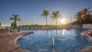 Une piscine entourée d’une terrasse en briques, agrémentée de chaises longues et de palmiers.