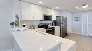 Une cuisine moderne avec des meubles blancs, un grand îlot central, des appareils en acier inoxydable et un plancher en bois clair.