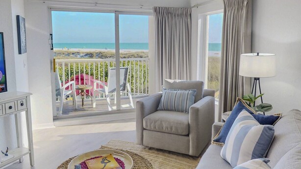 Un salon avec un canapé, un fauteuil et une vue sur la plage, accessible par une porte coulissante.