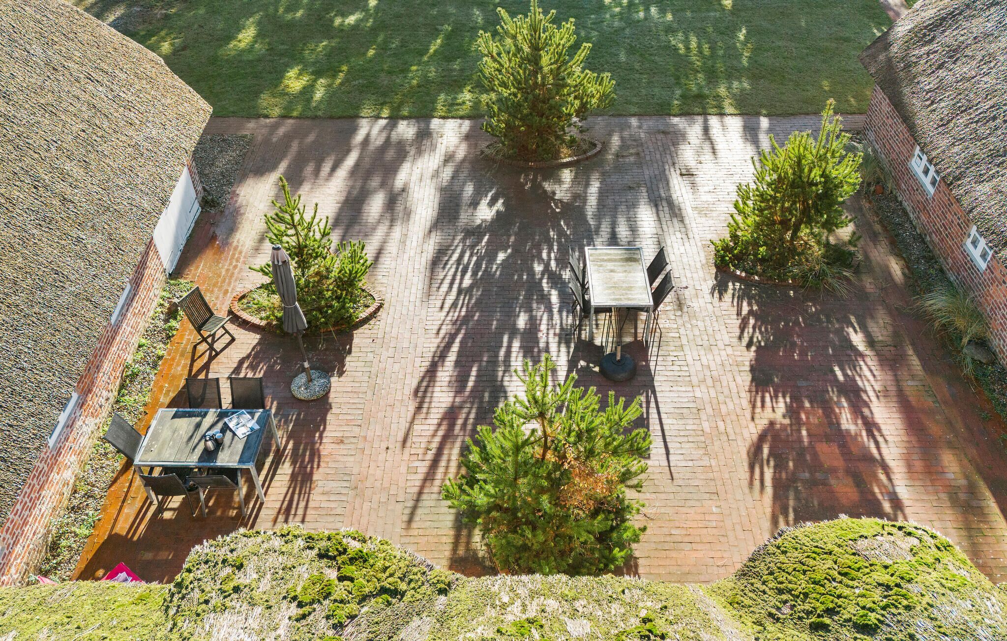Een terras buiten met bakstenen vloer, omringd door bomen en een bakstenen muur.