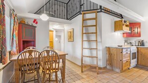 Une cuisine avec une table et des chaises en bois, une échelle et un escalier menant à un niveau supérieur.
