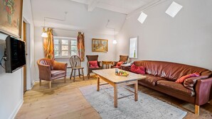 Un salon avec un canapé en cuir marron, des chaises en bois, une table basse en bois et un téléviseur fixé au mur.