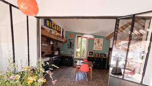 Cocina compacta con encimera de madera, comedor con mesa y sillas, y un arreglo floral sobre la mesa.