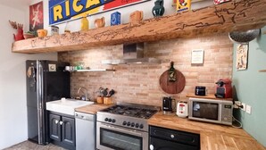 Una cocina de diseño rústico, con pared de ladrillo, estantes de madera y diversos electrodomésticos, incluyendo un refrigerador, estufa, horno y microondas.