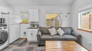 A compact kitchen with white cabinets, a gray sofa, and a wooden coffee table. - Cozy Tiny-Home with Big Heart! BBQ, 2Beds, WIFI, Pet Friendy! (Rockaway Beach)