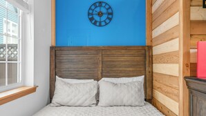 A bed with a wooden headboard, a blue wall, and a clock. - Cozy Tiny-Home with Big Heart! BBQ, 2Beds, WIFI, Pet Friendy! (Rockaway Beach)