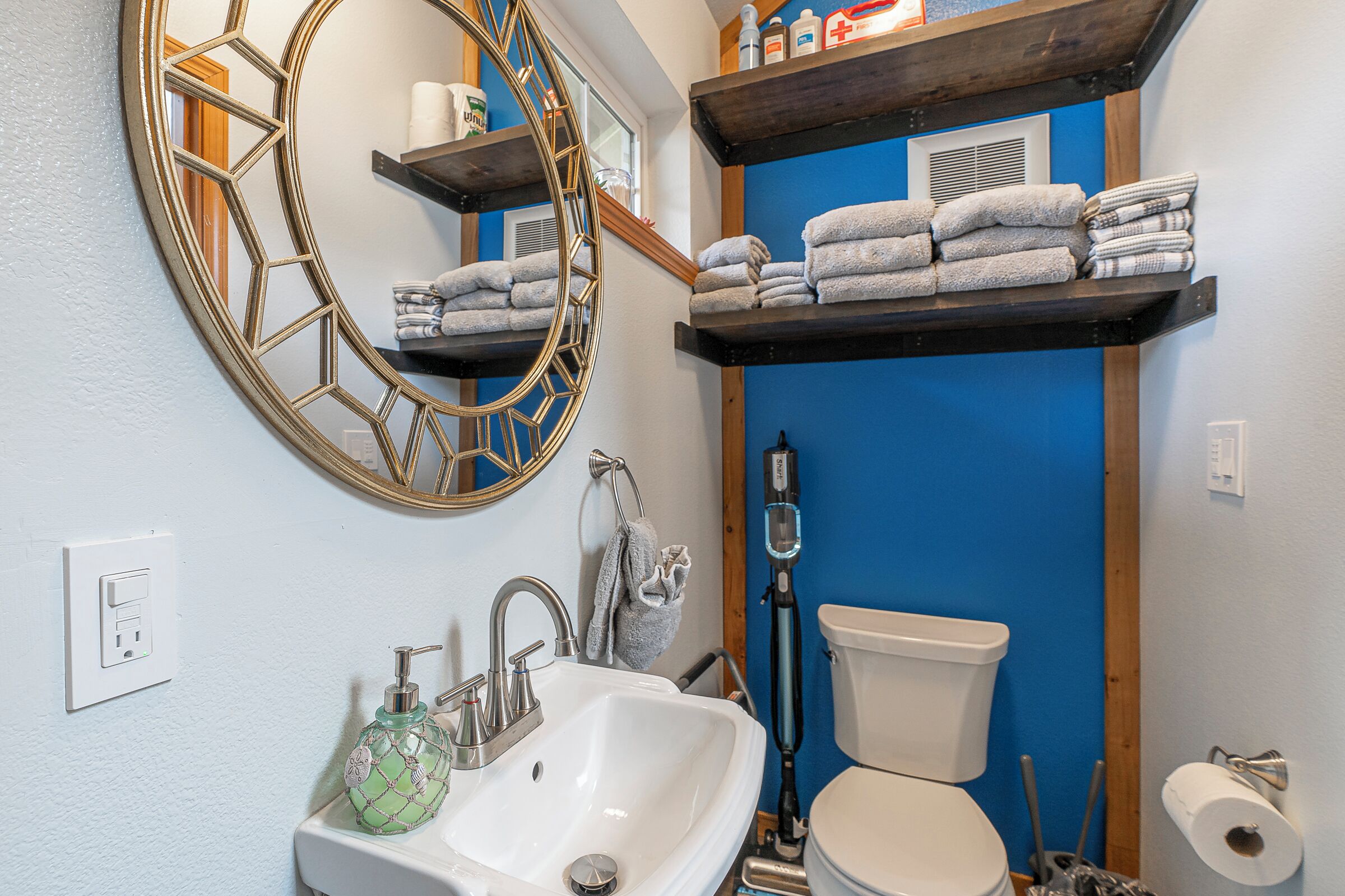 Un bagno con un lavandino bianco, uno specchio grande, un water e uno scaffale con asciugamani.