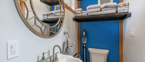 Un bagno con un lavandino bianco, uno specchio grande, un water e uno scaffale con asciugamani.
