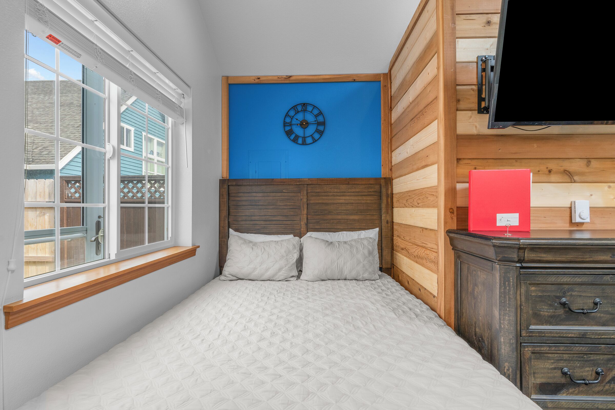 Ein Schlafzimmer mit Bett, Fenster, einer Wanduhr und einem Schminktisch.