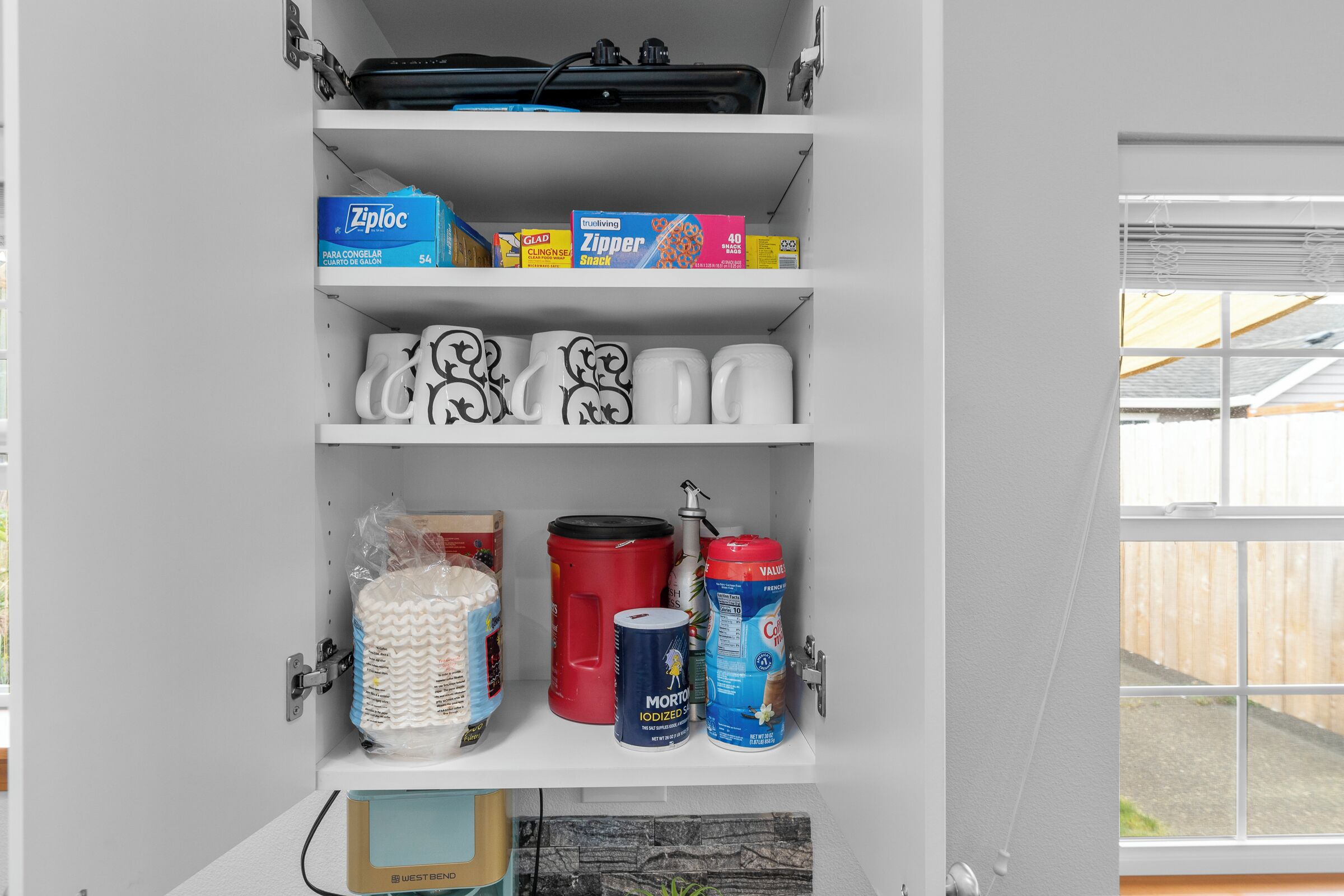 Un meuble de rangement doté d’étagères contenant divers objets, notamment des boîtes, des tasses et des récipients.