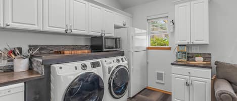 Cocina compacta con armarios blancos, microondas, refrigerador y lavadora.