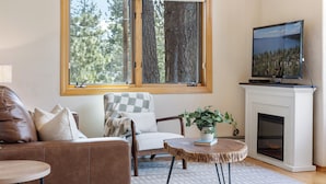 Ett vardagsrum med ett stort fönster, en öppen spis, en tv och en mysig sittgrupp.