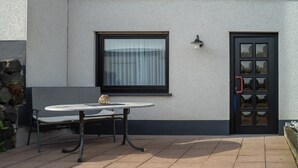 A patio with a table and bench, a window with curtains, and a door with a glass panel. - Apartment 'Juttis Bude' with Private Terrace, Shared Garden and Wi-Fi (Löhnberg)