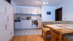 A modern kitchen with white cabinets, a wooden dining table, and a patterned bench. - Apartment 'Juttis Bude' with Private Terrace, Shared Garden and Wi-Fi (Löhnberg)