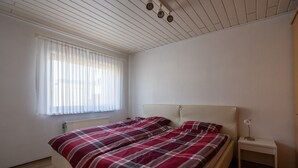 A bedroom with a bed, a nightstand, a window with blinds, and a ceiling with recessed lighting. - Apartment 'Juttis Bude' with Private Terrace, Shared Garden and Wi-Fi (Löhnberg)