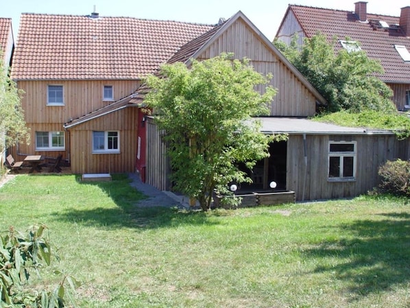 A wooden house with a red door, a small porch, and a tree in the yard.