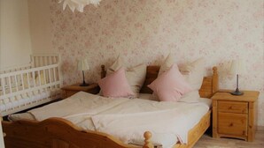A bedroom with a wooden bed, two bedside tables, a nightstand, a crib, and floral wallpaper. - Apartment 'Ferienhaus Kaline' with Private Terrace, Private Garden and Wi-Fi (Grebenhain)