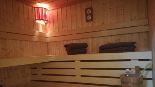 A sauna room with wooden benches, a towel rack, a wooden bucket, and a wall-mounted clock. - Apartment 'Ferienhaus Kaline' with Private Terrace, Private Garden and Wi-Fi (Grebenhain)