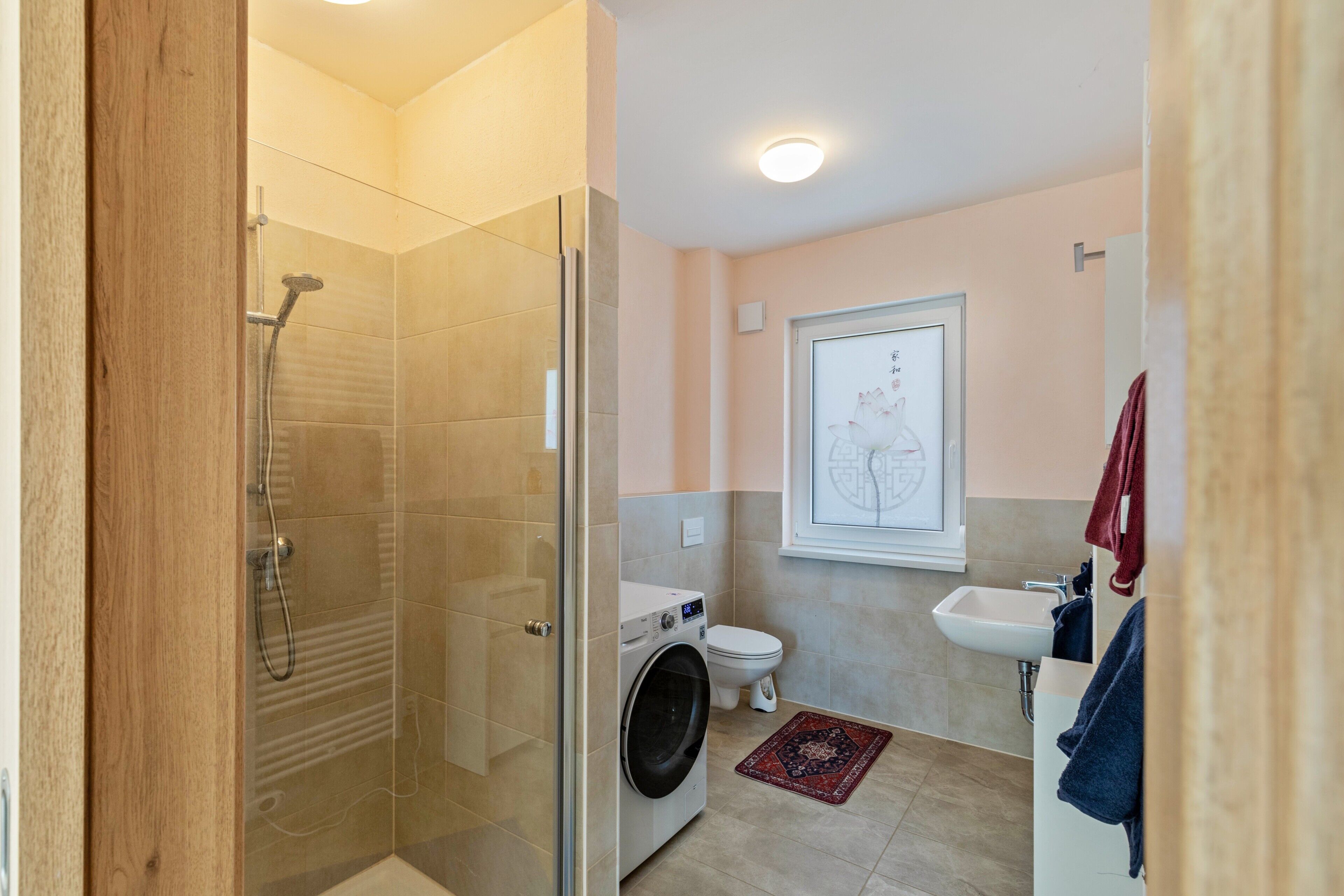 Een moderne badkamer met een glazen douchecabine, een wasmachine, toilet en wastafel.