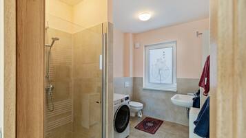Een moderne badkamer met een glazen douchecabine, een wasmachine, toilet en wastafel.