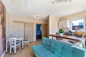 Un espacio habitable compacto con sofá, mesa de comedor, sillas, kitchenette y vista a través de una puerta abierta.