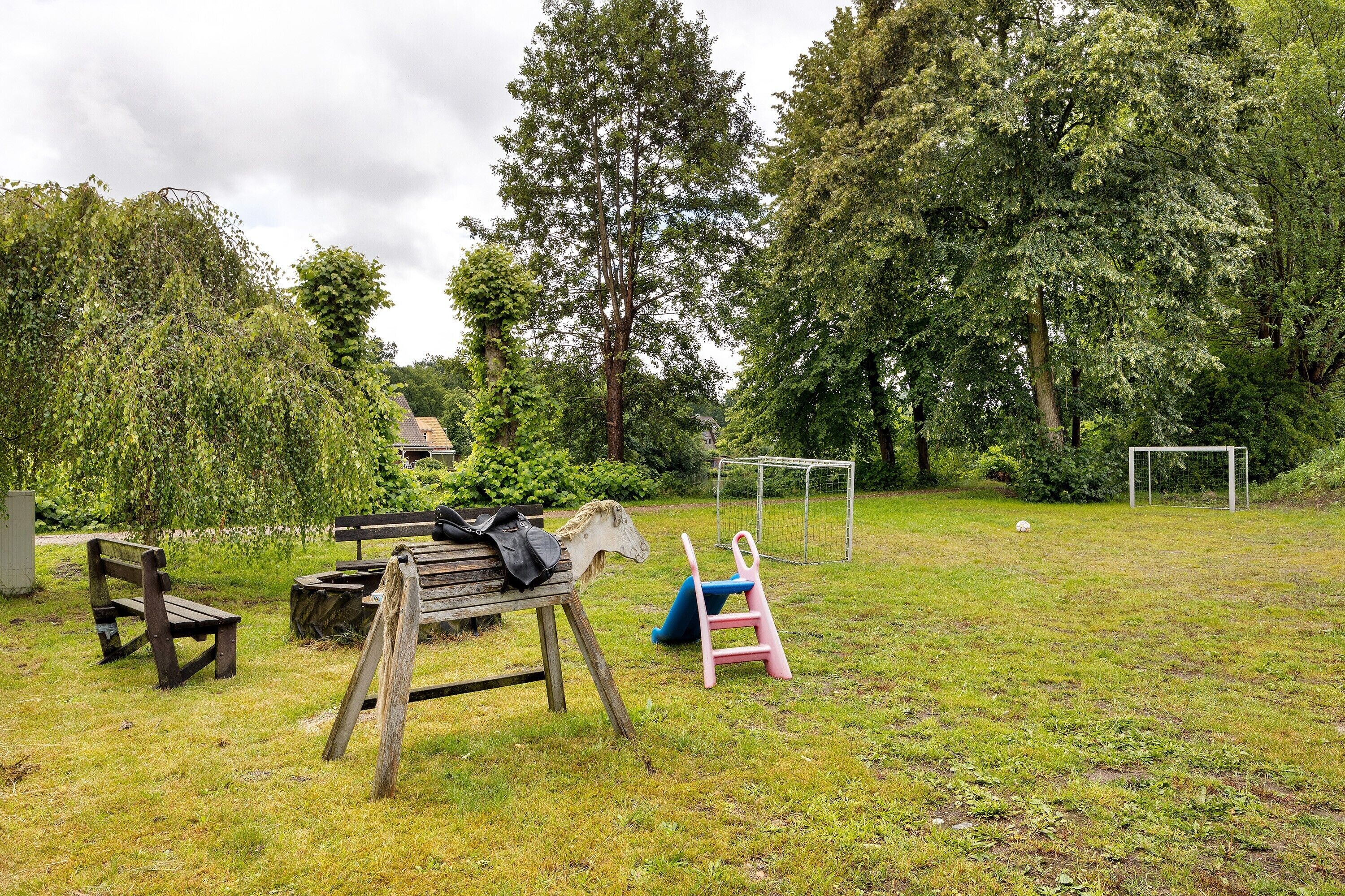 Een gazon met een houten bankje, een tafeltje en een voetbalkooi.