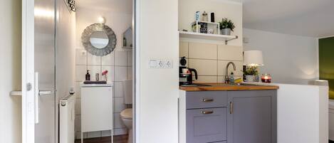 A compact kitchen with a built-in oven, a sink with a wooden countertop, and a grey cabinet with drawers.