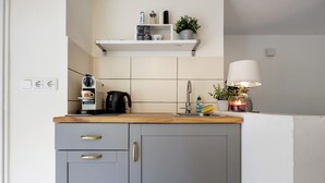 A kitchen with a coffee maker, kettle, and a shelf with various items.