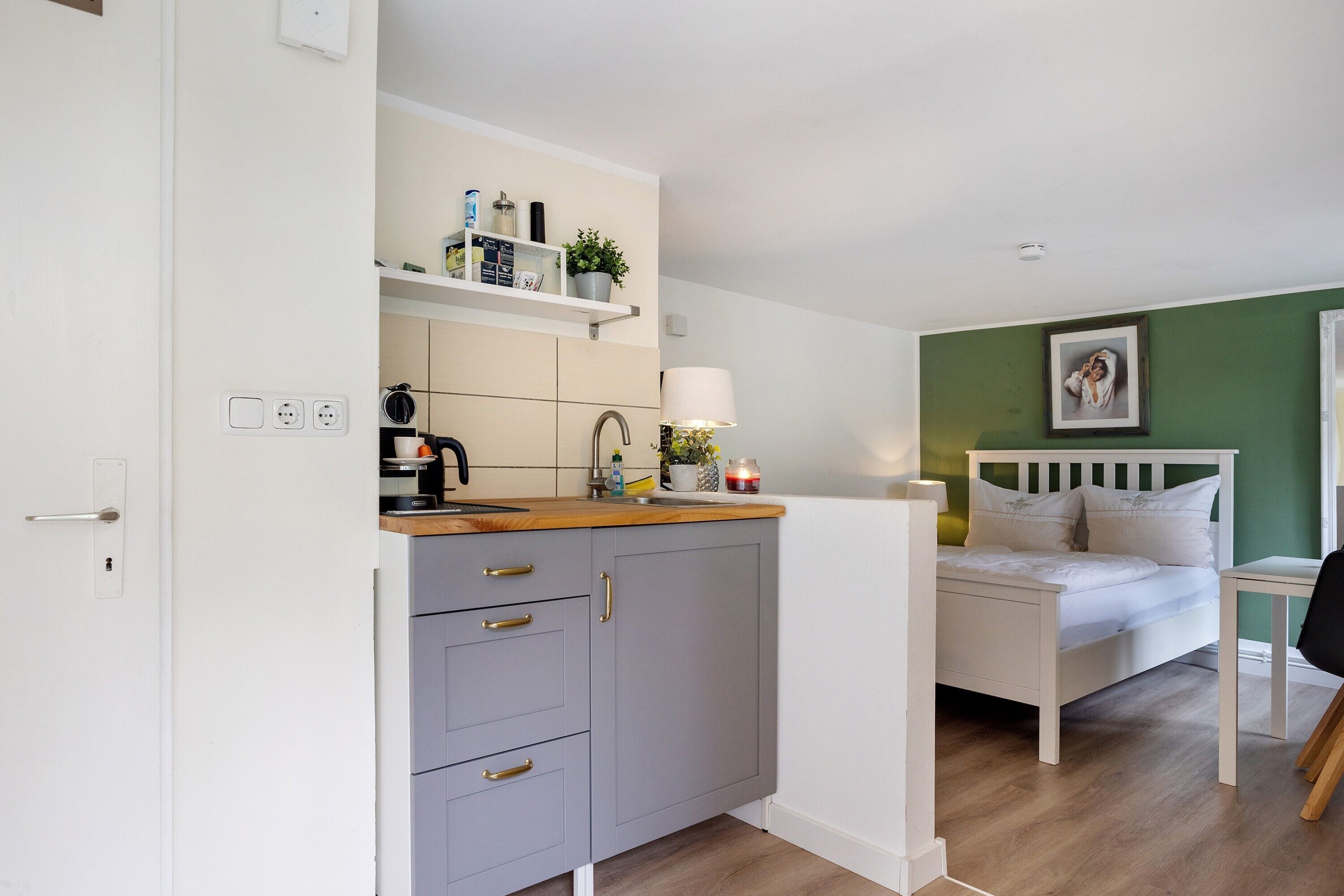 Ein kleines Zimmer mit Küchenzeile, einem Bett und einer grünen Wand.