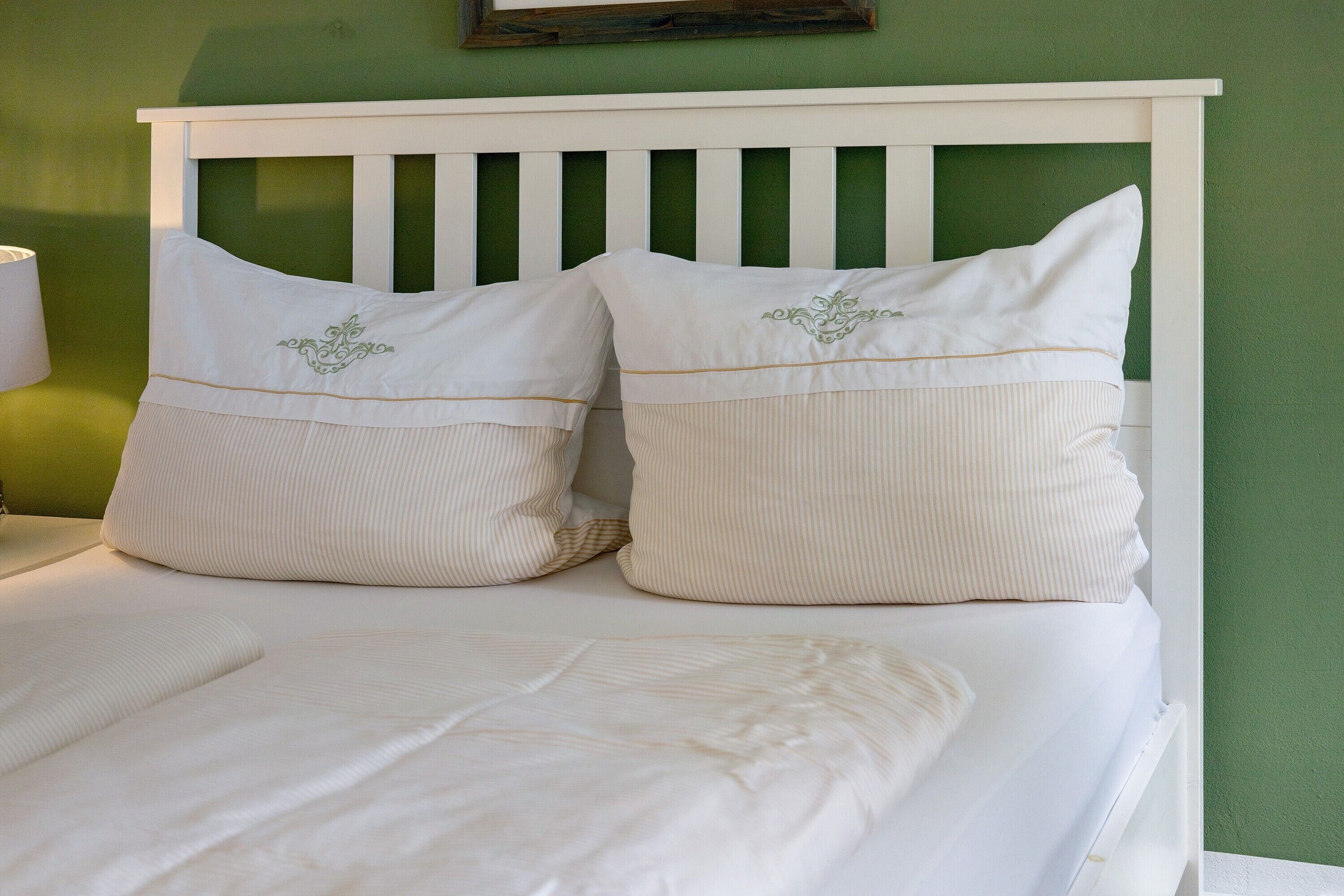 Ein Bett mit weißer Bettwäsche und zwei Kissen mit aufgestickten Motiven.