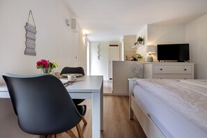 Ein modernes Schlafzimmer mit einem Bett, einem Schreibtisch, einem Sessel, einem Fernseher und einem Nachttisch mit einer Lampe.
