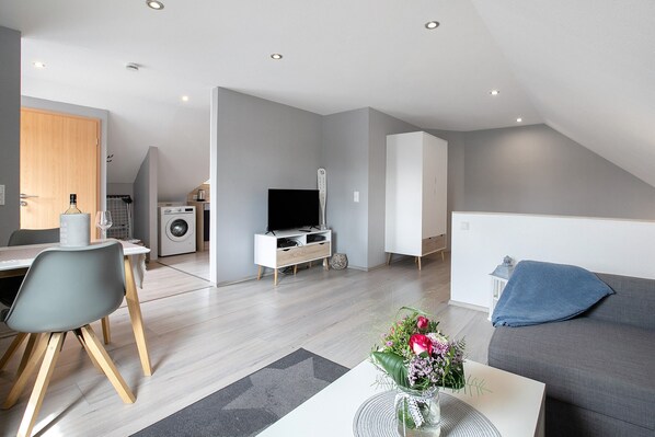 A modern apartment with a dining area, a living room with a sofa, a TV, and a kitchen area.