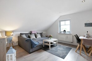 A modern loft bedroom with a sloped ceiling, a large window, a built-in desk, and a cozy seating area.