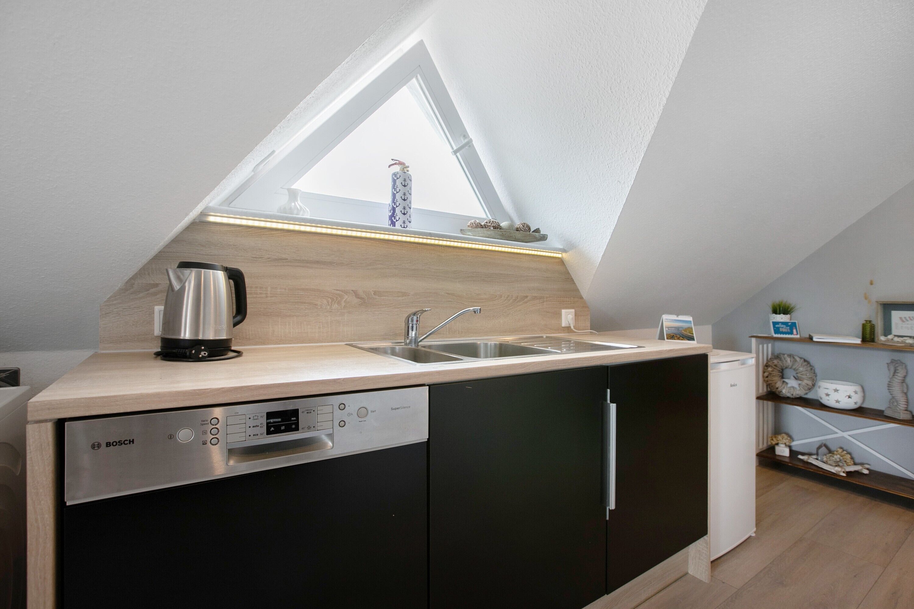 Une cuisine moderne équipée d’un lave-vaisselle Bosch, d’une machine à café et d’un évier placé sous une lucarne.