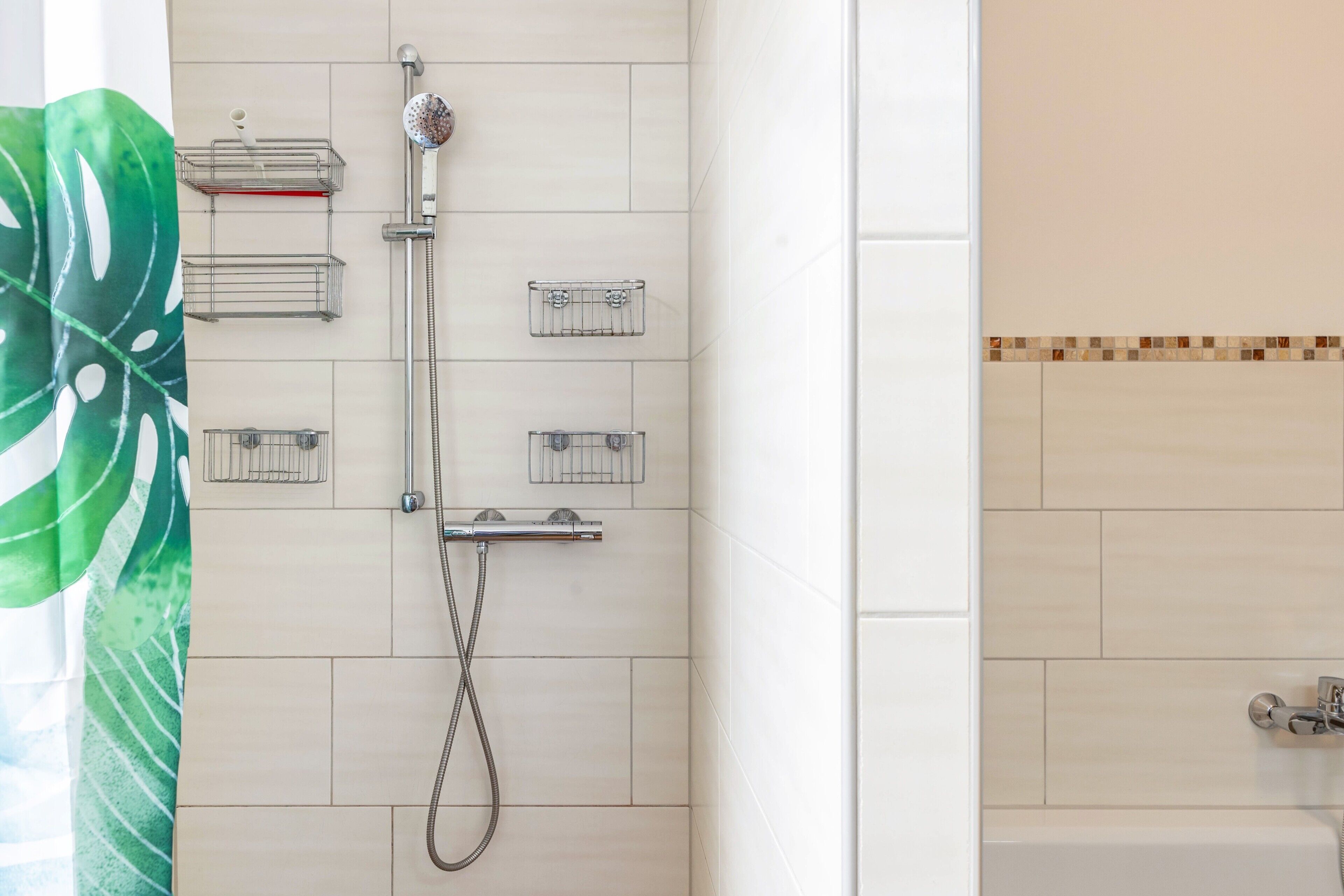Eine Dusche mit Handbrause, Duschwand und fest installierter Brauseköpfe.