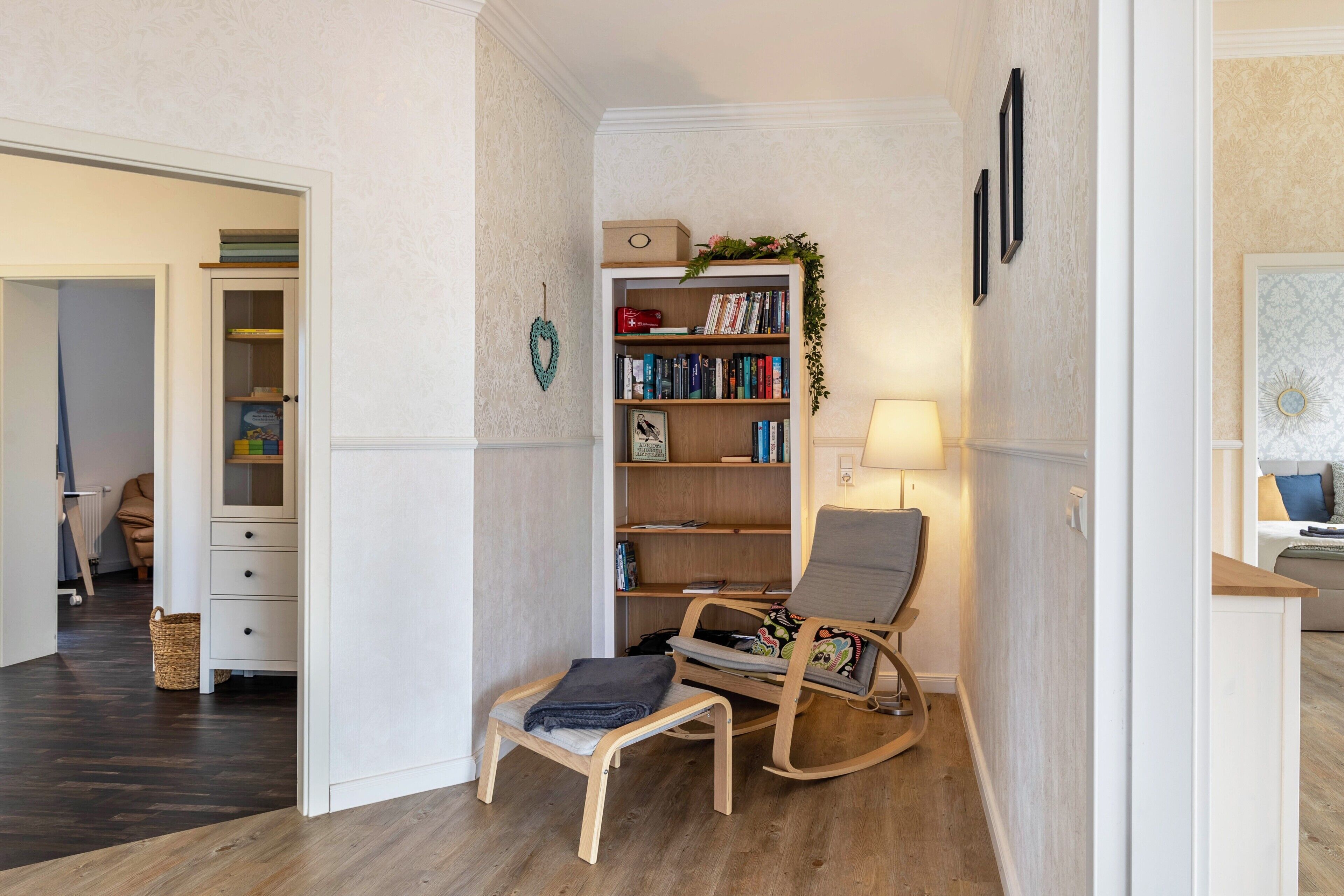 Una habitación con una estantería, un sillón mecedora, una mesita y una lámpara.