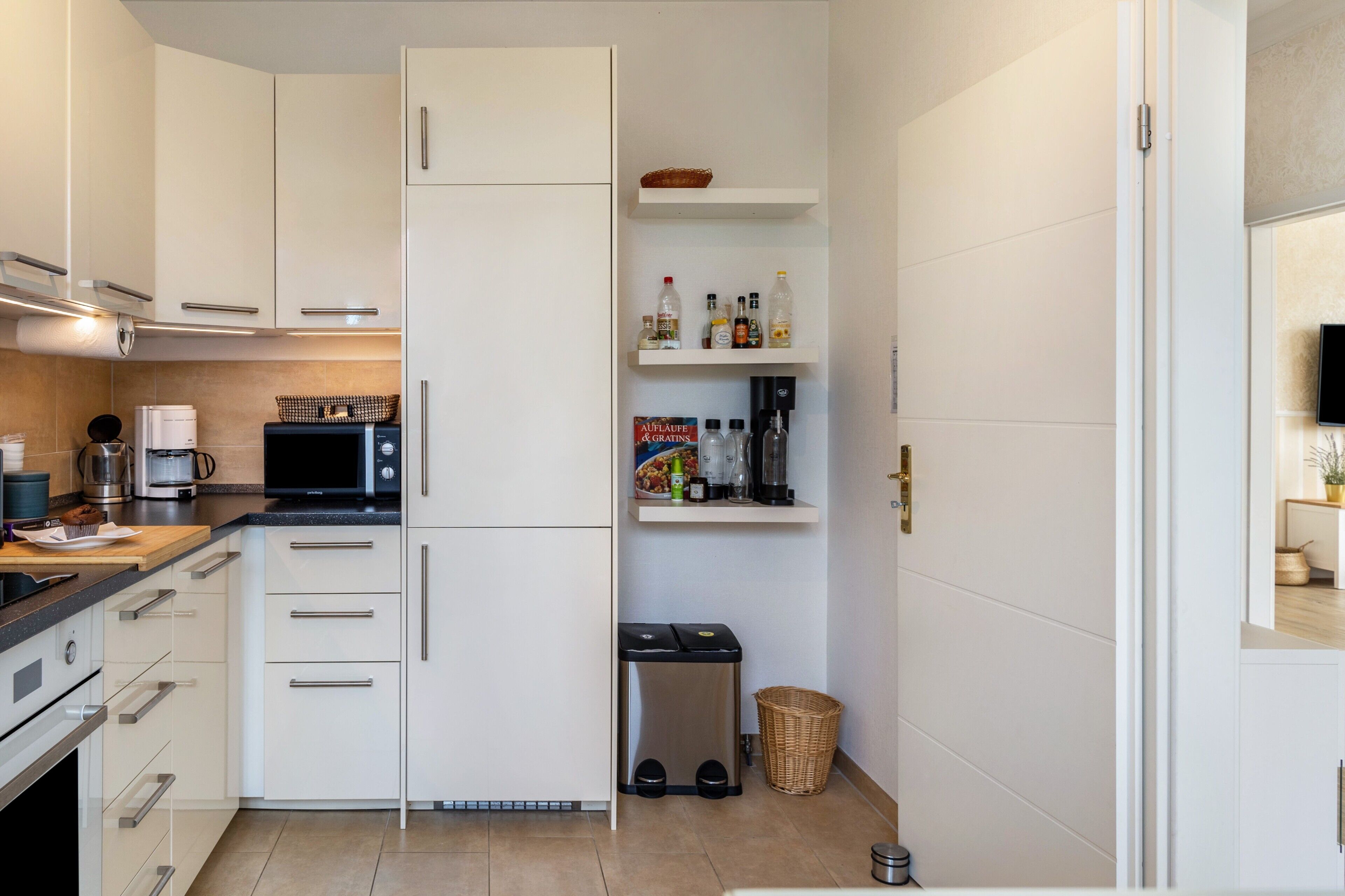 A modern kitchen with white cabinets, a black countertop, a microwave, a coffee maker, and a trash bin.