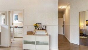 Un intérieur moderne avec un meuble blanc, un plancher en bois et un coin cuisine à l’arrière-plan.
